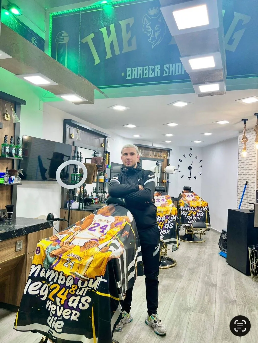 Uno de los barberos de brazos cruzados junto a los sillones del local, bajo el rótulo dorado